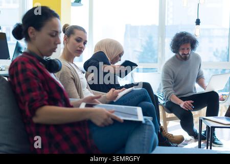 Side view of focused young colleagues sitting together in a row at a modern open-plan office, working diligently on laptops, digital tablets, and writ Stock Photo