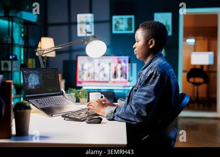 Black woman manages code and programs in artificial intelligence and machine learning on her laptop, African American female freelancer uses her personal computer to guarantee cyber security Stock Photo