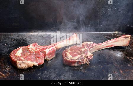 Fresh tomahawk steaks just put to roast on a metal flat bbq grill. Stock Photo