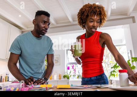 African American couple standing at kitchen counter organizing papers with smoothie and plants. Modern, home, lifestyle, notes, markers, daylight, orc Stock Photo