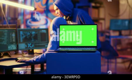 Green screen laptop in bunker with graffiti walls left behind by hackers to act as decoy. Mockup device running script pinging wrong location to cybercriminal law enforcement chasing them. Stock Photo