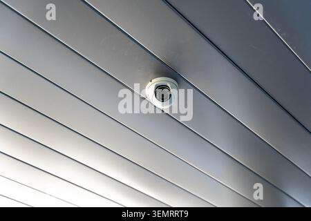 White dome security camera mounted on a metal ceiling for monitoring and protection Stock Photo