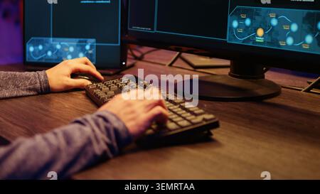 Hacker in secret underground shelter typing on keyboard, writing lines of code on computer, trying to get past security systems with virus, with scammer working on hacking script, close up shot. Stock Photo