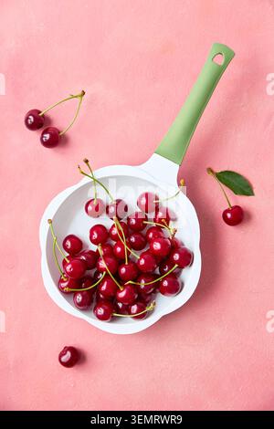 Ripe red cherries in mini frying pan on pink pastel background, top view Stock Photo