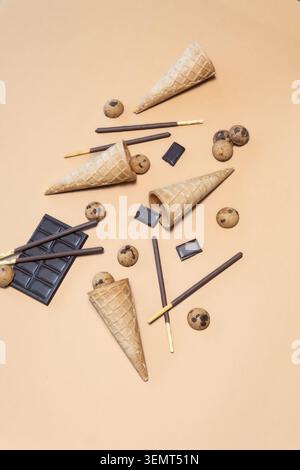 Assorted sweet treats including waffle cones, chocolate sticks, cookies, and chocolate bars on a beige background. Stock Photo