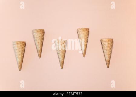 A row of five small ice cream cones on a beige background. All cones have the same size and shape. The single image. Stock Photo