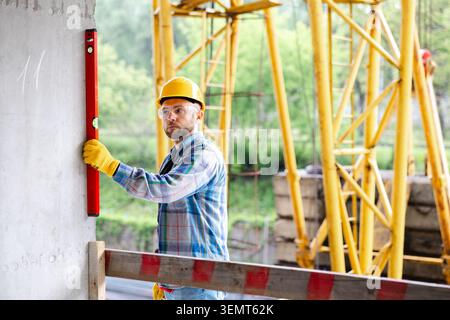 Skilled construction worker wearing safety gear checking the vertical alignment of a wall at a construction site using a spirit level Stock Photo