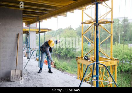 Construction worker wearing hardhat and safety glasses, managing a cable on a building site in rainy weather Stock Photo
