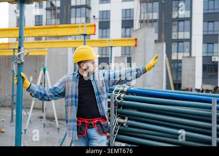 Construction worker in hard hat and safety glasses supervising building site development, extending arm measuring or indicating Stock Photo