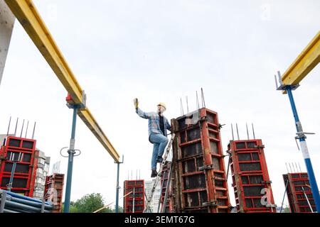 Construction worker in hard hat and safety glasses climbing ladder, setting metal formwork for a reinforced concrete column Stock Photo