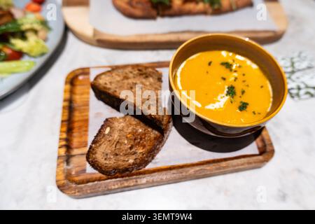 Creamy pumpkin soup served with toasted bread on wooden board in modern restaurant setting Stock Photo