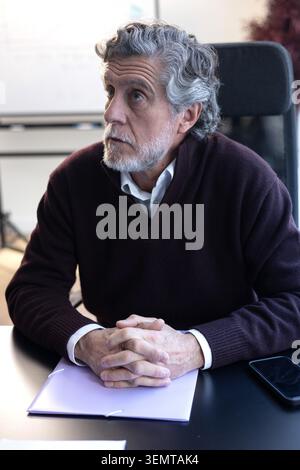 Senior man with gray hair and beard sitting at a desk, contemplating a thought Stock Photo