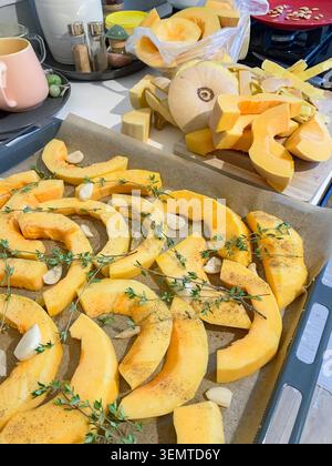 Vegetables including pumpkin are prepared on a baking tray ready to bake in the oven. The tray is lined and set on a stove surface. Stock Photo