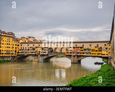 The iconic Ponte Vecchio, a medieval stone arch bridge lined with historic merchant buildings in warm ochre and terracotta tones, spans the Arno River Stock Photo