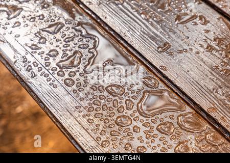 Raindrops forming diverse patterns on a wet wooden table, creating a textured background with natural moisture Stock Photo