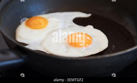 Two fried eggs with bright orange yolks cooking in a black frying pan. Close up. Stock Photo