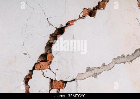 Wall with a large diagonal crack revealing old red bricks underneath, symbolizing damage, decay, and structural issues Stock Photo