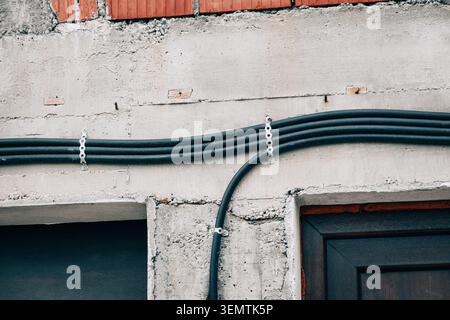 Electrical cables fastened on an concrete wall and exposed bricks, representing urban utility infrastructure and repair work Stock Photo