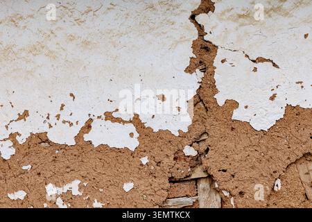Rough cracked wall plaster peeling, revealing a mud and straw texture underneath, showing concepts of decay and aging Stock Photo