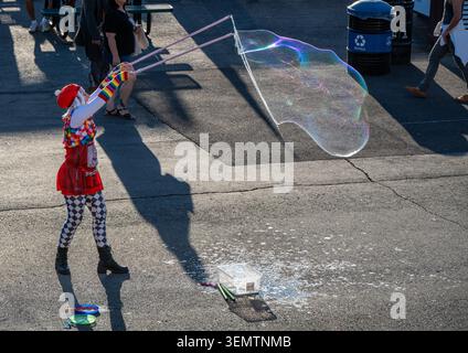 A colorful street performer creates a massive iridescent bubble during Pride month before a soccer match. Stock Photo