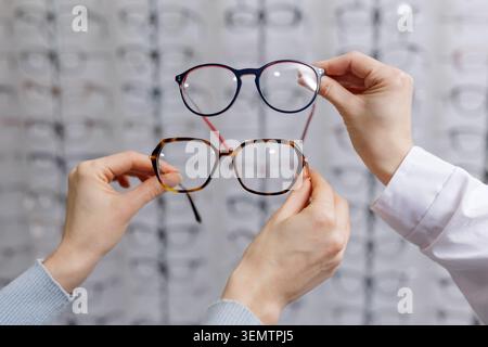 A person comparing two different styles of glasses in an optical store, highlighting the selection process for those with poor vision. Stock Photo