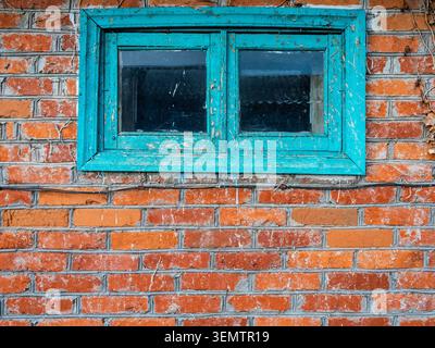 ivy-cleaned brick wall of old barn with little peeling window frame painted green in village Stock Photo