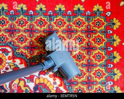 top view of vacuum cleaner brush cleans corner of Central Asian red wool carpet in apartment Stock Photo