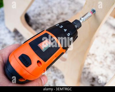hand using electric screwdriver assembles wooden furniture outdoors close-up Stock Photo