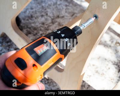 carpenter assembles wooden furniture using electric screwdriver outdoors close-up Stock Photo