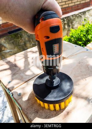 man cleans surface of bench from dust using brush and electric screwdriver outdoors close-up Stock Photo