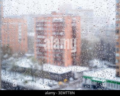 water drops from rain and melted snow on glass surface on home window and blured cityscape on background Stock Photo
