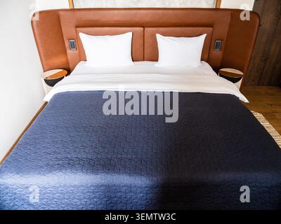 double bed with blue bedspread and leather headboard in hotel room Stock Photo