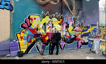 Stockholm, Sweden, may 17, 2026. Two street artists stand by a vibrant graffiti mural on a city wall, sharing tools and conversation while spray paint Stock Photo