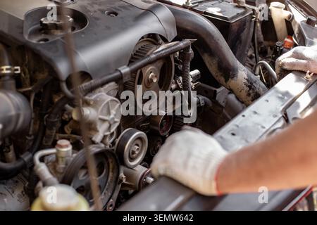 Mechanic loosens a belt tensioner while working under the car hood. engine maintenance, belt replacement, auto repair Stock Photo