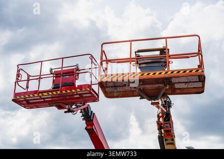 Industrial boom lift cages on hydraulic telescopic arms used for elevated building maintenance and high altitude construction works business Stock Photo