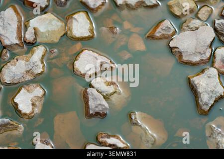 Small crushed limestone rocks and gravel submerged under murky muddy puddle water on construction site or environmental ecology area Stock Photo