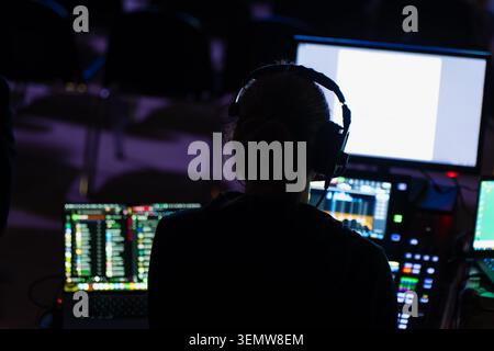 An audio visual specialist monitors multi screen production software on an interactive display terminal inside a tech control room venue station Stock Photo