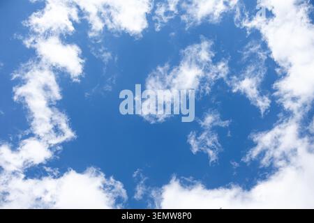 Blue Sky With Soft White Clouds. Bright blue sky with scattered white clouds, creating a clean, calm, open background for nature and weather concepts. Stock Photo