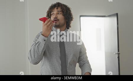 Man in shirt and tie holding red smartphone to mouth, gesturing with hand in building; confident sales pitch. Stock Photo