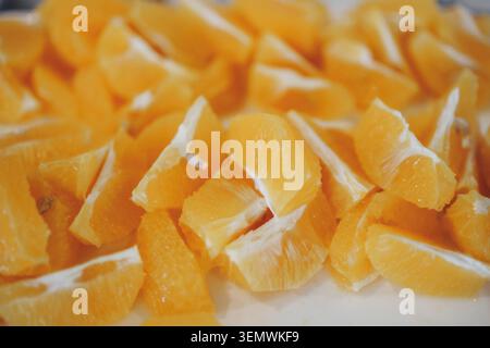 Bright orange segments pile on white surface. Fruit juicy and vibrant, freshly cut. Perfect for healthy eating or cooking visuals. Suggests freshness, Stock Photo