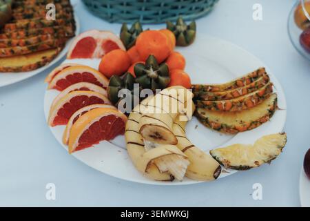 Colorful fruit platter arranged on a white plate. Sliced pineapple, grapefruit, bananas, and oranges. Bright, fresh, and inviting for healthy meals or Stock Photo