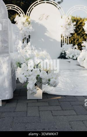 White blooms grace an elegant wedding arch. Soft sunlight illuminates delicate petals and draped fabric. The scene invites romance, quiet celebration, Stock Photo