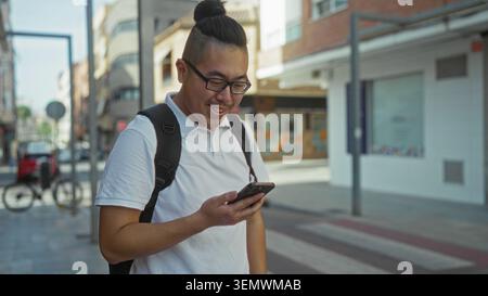 Man wearing glasses and white polo holding smartphone with visible hand and backpack on urban street beside storefront and bicycle rack, checking scre Stock Photo