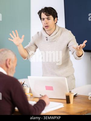 Quarrel between two managers - an elderly man and young man shout at each other, dissatisfied with their work Stock Photo