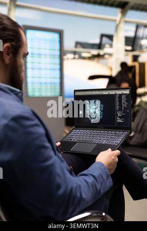 Male entrepreneur using AI assistant system on laptop in airport lounge, analyzing big data with machine learning algorithms. Corporate travel concept highlighting smart technology. Stock Photo