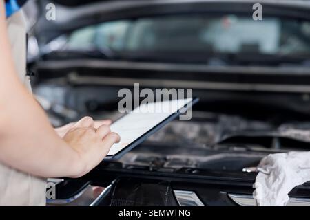 Licensed technician in garage using tablet to follow checklist while doing maintenance on car. Close up shot of expert in auto repair shop doing checkup on vehicle radiator Stock Photo