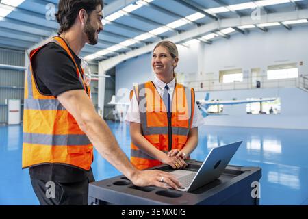Aviation professionals collaborating in an airplane hangar, a male engineer and a female pilot discussing maintenance data on a laptop, ensuring safet Stock Photo
