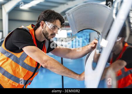Skilled engineer wearing safety glasses and a high visibility vest meticulously inspecting and working on a light aircraft engine in a professional av Stock Photo