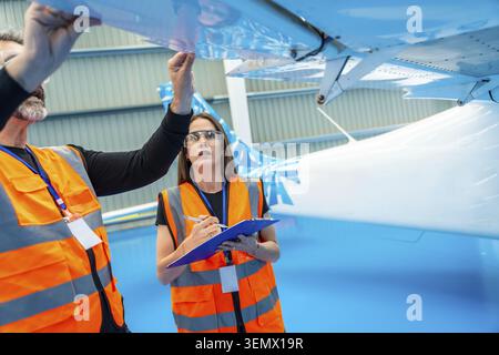Aviation engineers collaborating on a thorough inspection of an airplane wing inside a hangar, ensuring safety and quality control for aeronautical ma Stock Photo