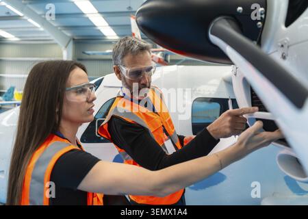 Two aerospace engineers wearing safety vests and goggles, carefully examining an airplane engine for maintenance and pre flight checks in an aircraft Stock Photo